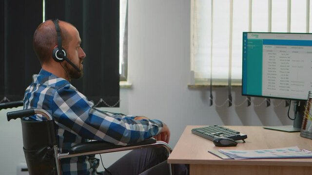Handicapped disabled operator sitting in wheelchair making telemarketing in business office. Immobilized, disabled, paralysed freelancer working in financial corporate building using heatset