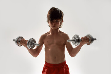 Little sportive boy child with muscular body looking focused at camera, lifting weights while standing isolated over white background