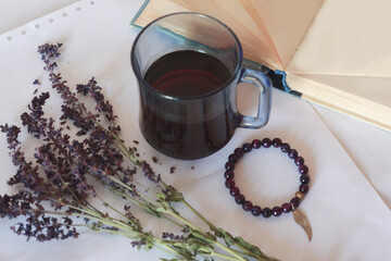 Blue transparent cup of black tea, beautiful dried flowers, natural purple agate bracelet, book with blank sheets on white paper.