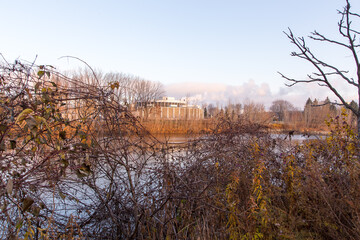Northern view of the St. Charles River bank with the circular Limoilou pumping station seen through dry shrubs in the background, Quebec City, Quebec, Canada