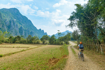 Fototapeta na wymiar Woman riding mountain bike on dirt road in scenic landscape around Vang Vieng backpacker travel destination in Laos Asia rock pinnacles green valley