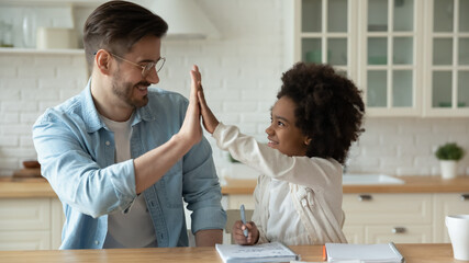 Smiling father and African American little girl giving high five, celebrating success, adorable girl with happy dad studying together, teacher supporting pupil, multiracial family, homeschooling