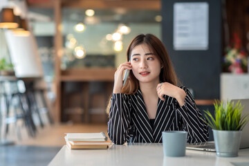 Happy young asian businesswoman working on laptop and talking on smartphone.