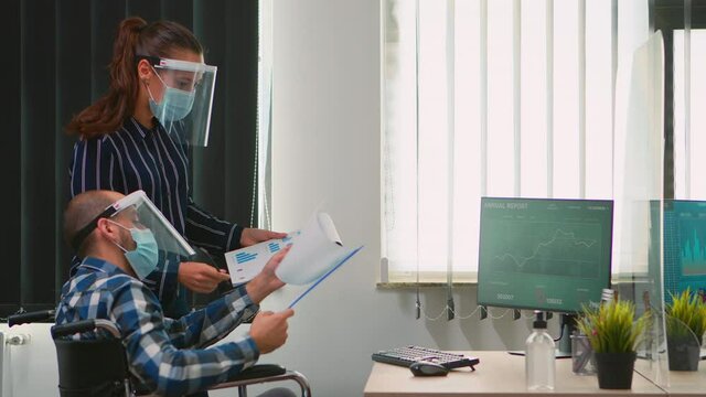 Business people wearing protective mask in new normal office making strategy, businessman sitting in wheelchair Team working in profesional workspace in corporate company during covid-19 pandemic.