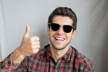 Portrait of a cheerful young man in black sunglasses with a big smile showing a thumb up gesture 