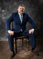Mature businessman in a suit sitting on chair studio portrait.