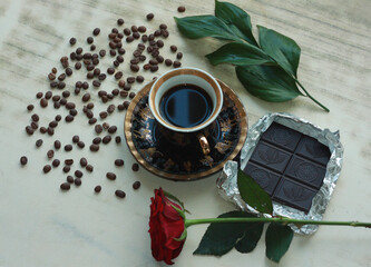 Vintage beautiful cup of hot coffee, bright red rose, green leaves, scattered coffee beans and dark...