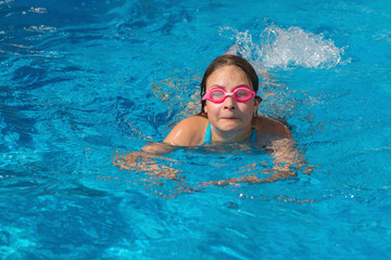 Girl in glasses swim in the blue swimming pool.