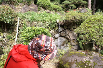 小さい滝を見つめる赤いパーカーを着た帽子をかぶった人