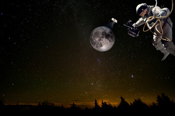 Astronaut in outer space explores the moon, illuminating it with pocket flashlight. Collage with...
