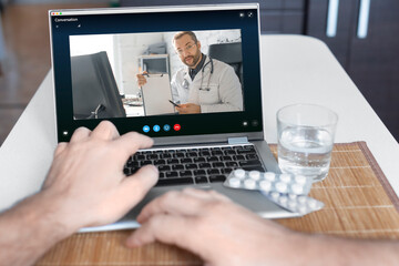 Close-up view of a patient's hand in front of a laptop during an online consultation with a doctor.