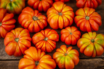 Red ribbed tomatoes on a wooden background. American or Florentine variety Nina. Food on the table top view. Autumn harvest of vegetables similar to flowers and pumpkins.Ribby tomato.