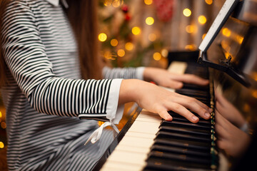Close-up shot of girl`s hands on keyboard of a piano with christmas lights on the background. Christmas and New Year holidays © Vitalii