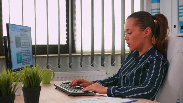 Business woman typing on computer in modern office room. Hispanic entrepreneur working in professional workspace, in personal corporate company writing on computer keyboard looking at desktop