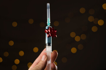 Mano sosteniendo una jeringuilla, vacuna covid-19, coronavirus, regalo de navidad con lazo rojo