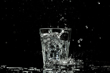 Splashes and drops of water in a glass are isolated on a black background. place for text