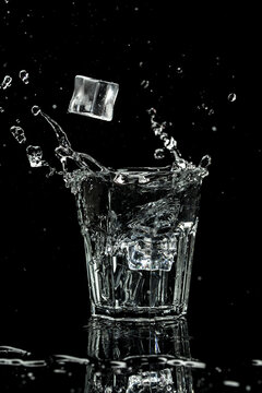 Close up view of the ice cubes splash in water are isolated on a black background. vertical image, place for text