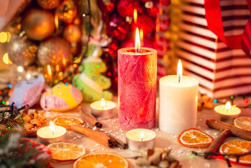 Obraz na płótnie Canvas Big red and white candles on the table with beautiful Christmas decorations around. Sticks of cinnamon, dried orange, self made christmas tree baubles, branches of the christmas tree on the table