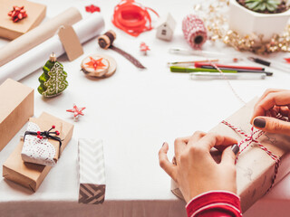 Naklejka na ściany i meble Table with Christmas decorations. Woman draws New Year symbols on craft paper and wraps presents. Flat lay with copy space.