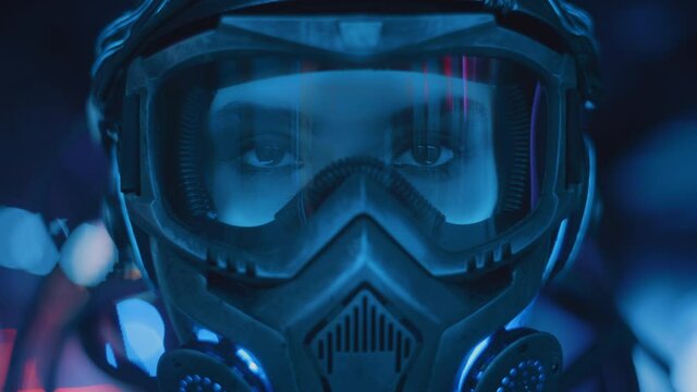 Close-up portrait female soldier of future in fiction helmet open her eyes backlit with neon city street lights. Cyborg girl in futuristic combat suit. Cyberpunk warrior, bright night illumination