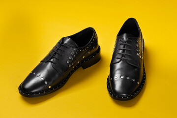 Stylish leather female shoes of black color with rivets on a yellow background.