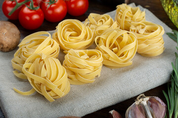 Raw pasta tagliatelle with fresh tomatoes, peppers, asparagus beans, spices and cheese on wood background.