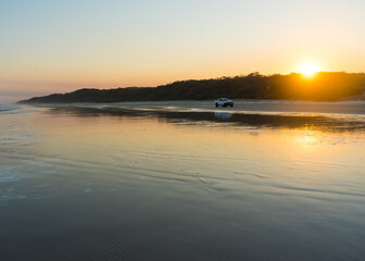 Four wheel drive vehicle driving on the beach at sunset