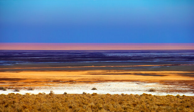 Beautiful nature view, surface of Namak lake with multicolor stripes of white salt crust, yellow sand and blue water at the background of sunset sky in Maranjab desert near Isfahan, Iran, Middle East