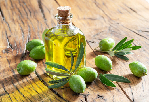 Green natural olives with bottle of olive oil on a vintage old wooden table.
