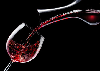 Red wine is poured into a wine glass on a black background.
