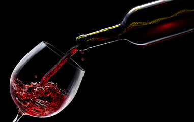 Red wine is poured into a wine glass on a black background.