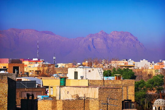 Beautiful city scape, old and modern houses at the background of purple barren mountain range, haze or smog and blue sky at evening, view from the roof, Isfahan (Esfahan), Iran (Persia), Middle East