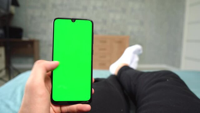 man uses phone with green screen lying on bed