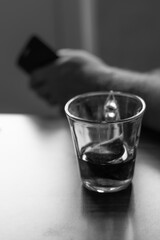 There is a glass of unfinished tea on the table. A man with a phone is nearby, a blurred background. Loneliness and problems