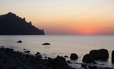 Fototapeta premium Early morning before sunrise on the Crimean coast. Beautiful view of the silhouette of Karadag mountain and pink dawn over the sea