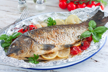 whole baked carp in foil with lemon in the oven on a wooden table, horizontal