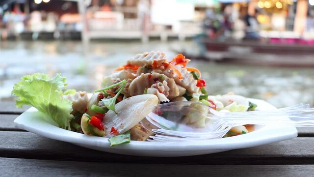 The spicy vietnamese sausage salad on dish with blurred of motion boat at background, Khlong Lat Mayom Floating Market, Thailand.