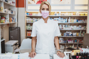 Young and attractive female pharmacist with face protective mask working in drugstore. She is confident and serious. Covid-19 open for business concept.