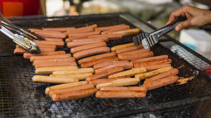 Grilling full of raw fresh sausage on barbecue grill and turned it using tongs on a summer picnic. Preparation of roasted chicken hot dogs on a hot grill stove. Selective focus.