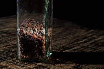 Tibetan black salt in a glass jar close up. Salt on a black, old shabby board. Contrasting dramatic light as an artistic effect. Free space and copy space for text near condiments.