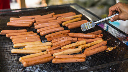 Grilling full of raw fresh sausage on barbecue grill and turned it using tongs on a summer picnic. Preparation of roasted chicken hot dogs on a hot grill stove. Selective focus.