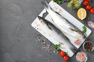 Raw fish mullet with ingredients and seasonings on white plastic board on dark background with place for text. Top view