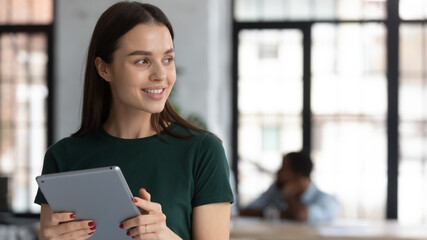 For a minute. Happy smiling young woman engaged in working at digital pad in office workspace throwing a look aside answering colleague question sharing good news taking pause to think, copy space