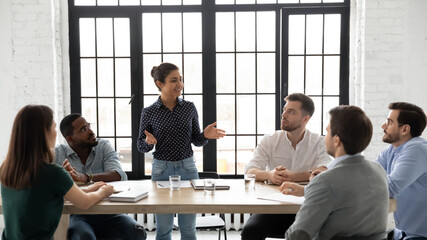 Business coaching. Friendly indian female coach delivering training to diverse group of young employees, capable millennial mixed race woman tutor explaining sales strategy to multiethnic intern team