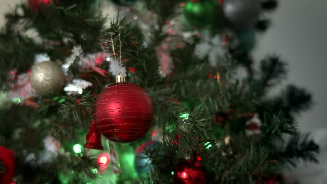 Close-up of man's hands decorating Christmas tree with balls on the background of bright festive lights. Decorating a Christmas tree with ornaments and lights.