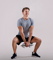 Strength workout concept. Positive young sportsman with dumbbell doing squat on light studio...