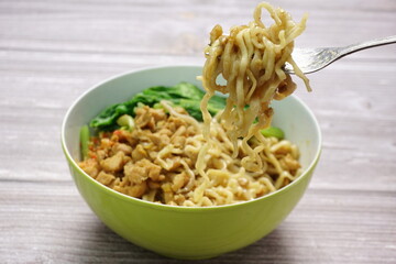 Mie Ayam or Indonesian chicken noodles topped with sweet sauce chicken, mustard greens and chili sauce on wooden background as a local street food
