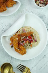 Top view of Ebi Furai (Udang Goreng Tepung) with brown rice and Sambal Matah, one of chili sauce from Indonesia. White plate in grainy texture background. Selective focus
