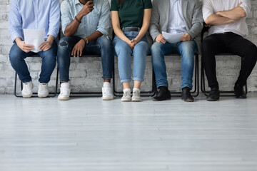 Fototapeta na wymiar Close up cropped shot of multiethnic group of young job applicants sitting in row at corporate office corridor preparing waiting for interview with hr feeling worry calm confident patient, copy space