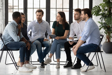 Brainstorming in narrow circle. Concentrated diverse teammates sitting on chairs close together...